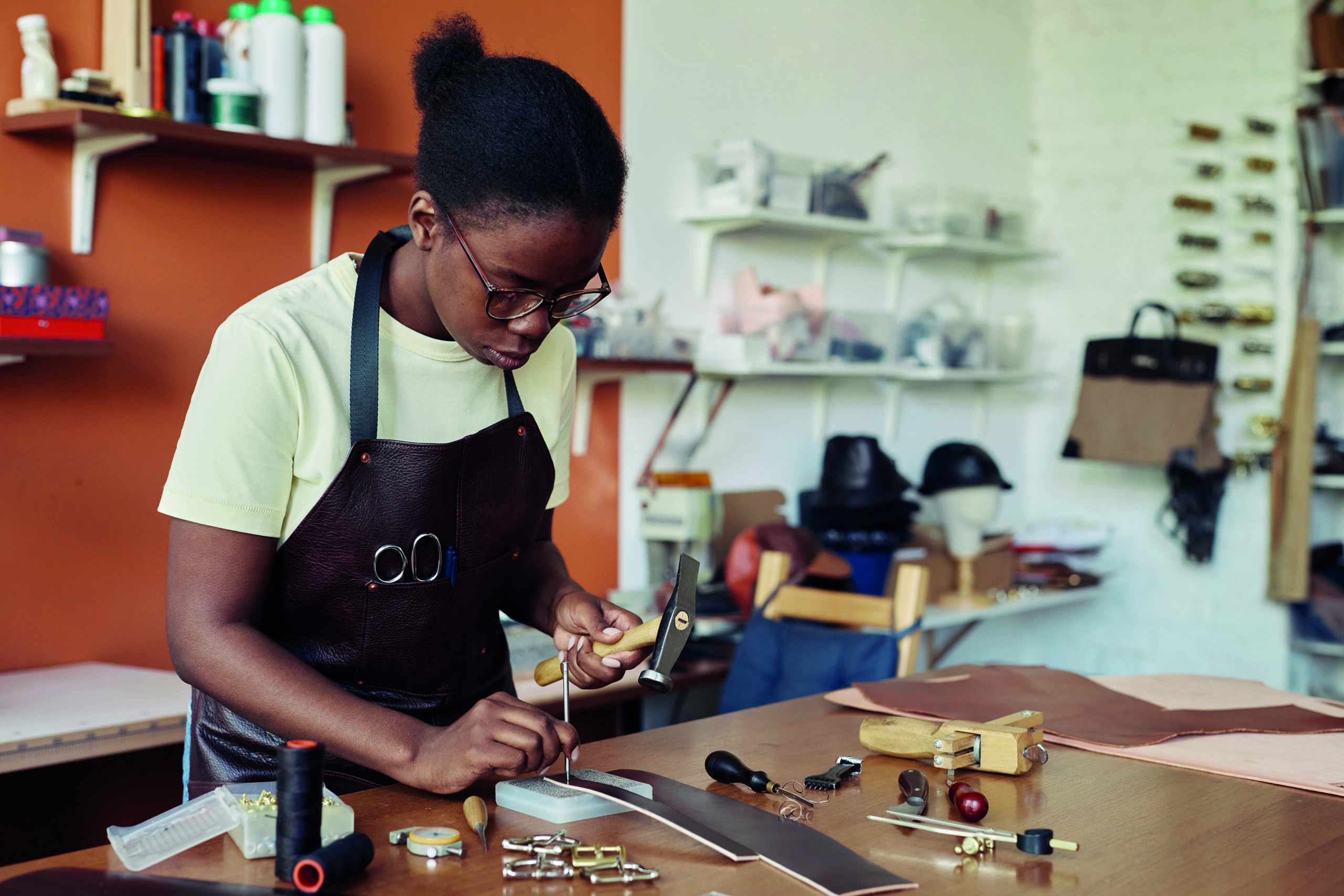 Portrait of black of female artisan punching holes in handmade leather belt at workshop, copy space